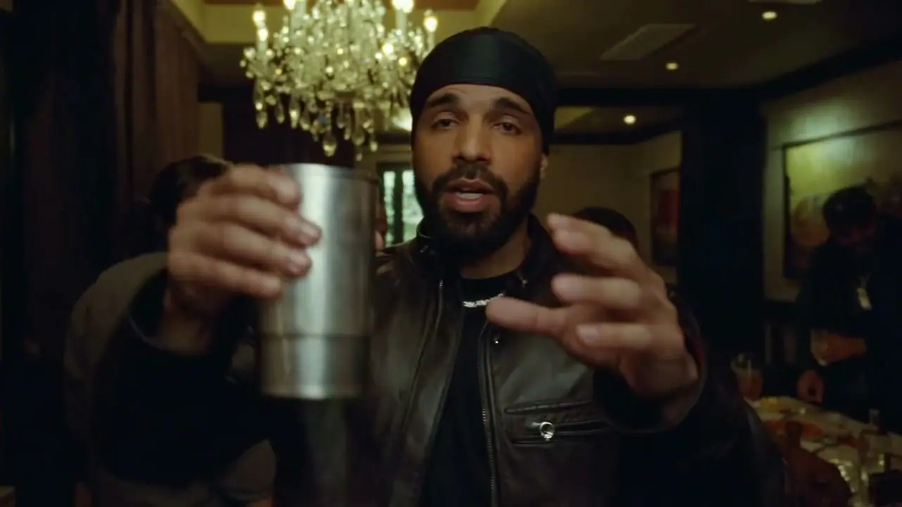 A performer in a dark jacket holding a cup in a warmly lit room